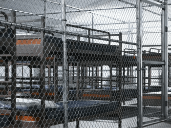 Empty detention beds behind prison fencing